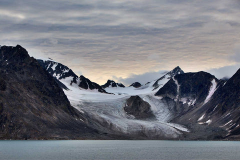 Blue glacier flowing down from snow-capped peaks with rugged dark mountains in Svalbard, fine art landscape photograph by Peter Cox