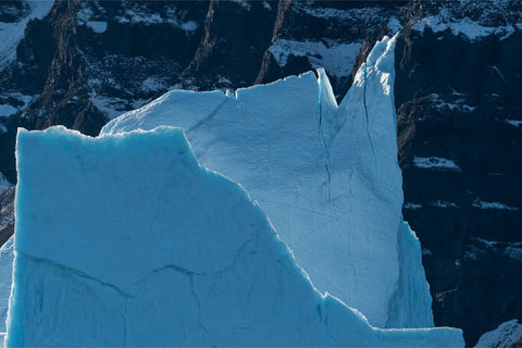 Massive blue iceberg with jagged peaks against snowy mountains, Scoresby Sound, Greenland — fine art landscape photograph by Peter Cox