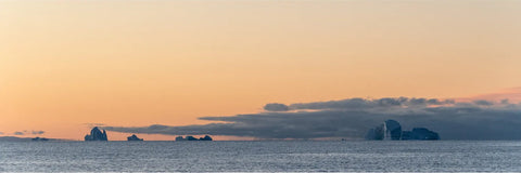 Icebergs silhouetted against a warm peach sky at dusk in Scoresby Sound, Greenland — fine art landscape photograph by Peter Cox