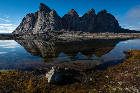 Sharp angular mountain peaks reflected perfectly in still clear water with mossy green foreground in Scoresby Sound, Greenland