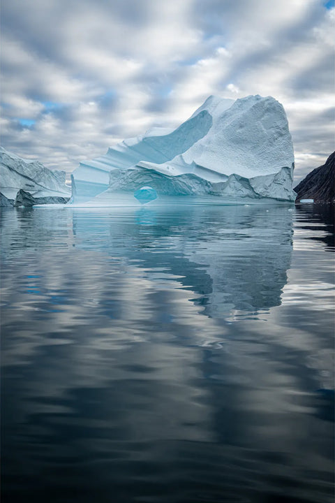 Iceberg with glacial blue arch reflected in calm waters, Scoresby Sound, Greenland, fine art photograph by Peter Cox