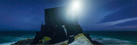 Fastnet Rock lighthouse beam blazing against a star-filled night sky over the dark Atlantic Ocean off the Cork coast