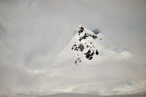 Pointed mountain peak with dark rock and snow emerging through cloud cover at Charlotte Bay on the Antarctic Peninsula