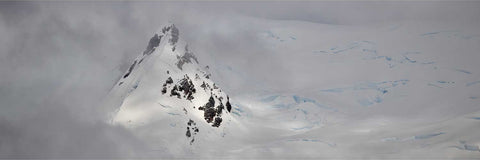 Rugged Antarctic peak at Charlotte Bay with icy blue and dark rock contrasts, light breaking through dense cloud above