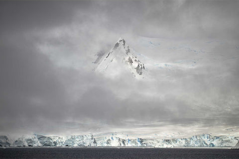 Solitary Antarctic peak piercing through mist at Charlotte Bay with glaciers and soft icy tones in an ethereal polar atmosphere