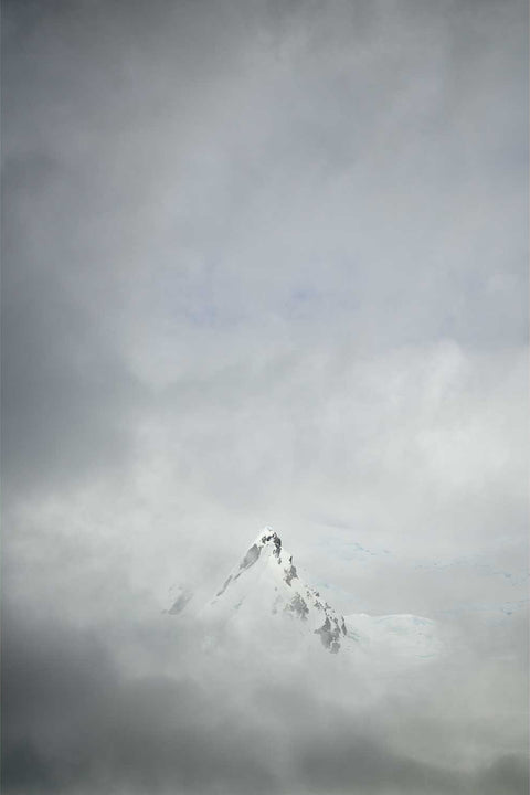 Mountain summit floating above a thick layer of fog at Charlotte Bay on the Antarctic Peninsula in soft grey and white tones