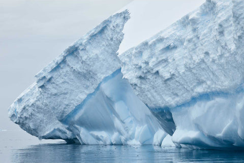 Two angular iceberg faces with deep blue compressed ice layers near Cuverville Island, Antarctic Peninsula — fine art landscape photograph by Peter Cox