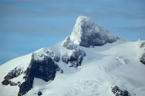 Rugged snow-crowned mountain peak rising sharply above glacial slopes at King Haakon Bay in South Georgia against pale blue sky