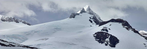 Snow-capped peak rising above a glacier at King Haakon Bay in South Georgia with jagged summit against cloudy skies