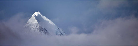 Snow-covered mountain summit breaking through a band of cloud at St. Andrew's Bay in South Georgia against a blue sky