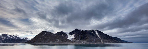 Rugged snow-dusted mountains of Spitsbergen meeting calm Arctic waters under dramatic clouds, Svalbard