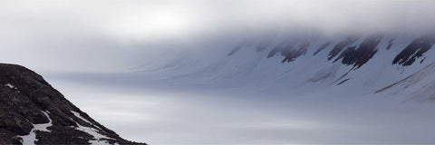 Snow-covered glacier flowing through a mountain valley beneath low-hanging clouds, Svalbard