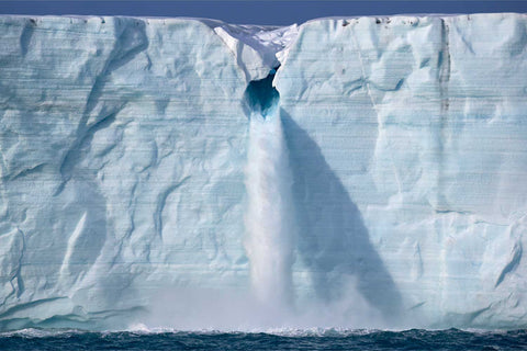 Meltwater rushing from the towering ice wall of Brasvellbreen glacier into the Arctic sea, Svalbard