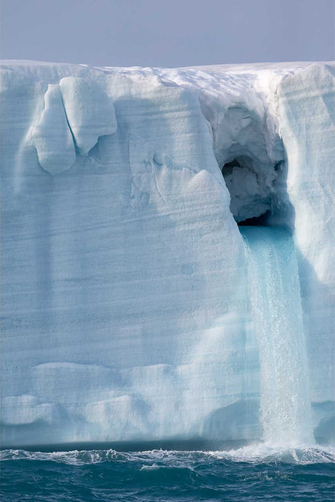 Meltwater cascading from a towering glacier face in Svalbard, resembling an ice giant exhaling — fine art landscape photograph by Peter Cox