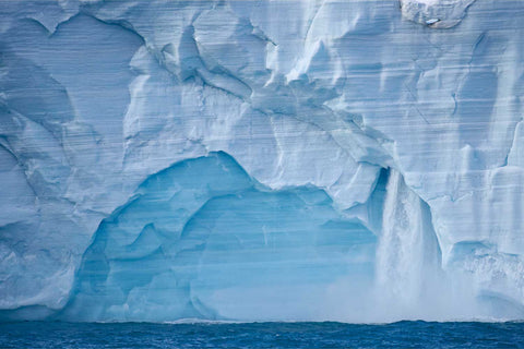 Vast ice arch in the Brasvellbreen glacier face with meltwater cascading into the Arctic sea, Svalbard