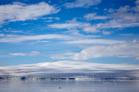The Nordaustland Ice Cap glacier face stretching along the horizon in Svalbard with calm Arctic waters and vivid blue sky