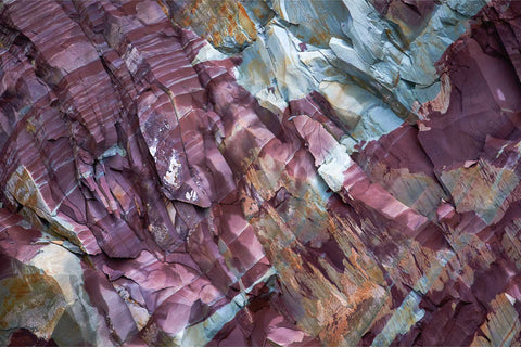 Abstract close-up of richly coloured layered rock showing deep purple, slate blue and rusty orange mineral bands in Svalbard