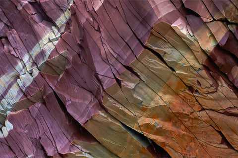 Close-up of layered rock formations with vivid purple, orange and ochre bands in Murchisonfjorden, Svalbard