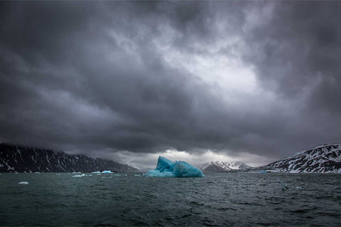 Blue iceberg floating beneath dark storm clouds at Lilliehookbreen glacier, Svalbard