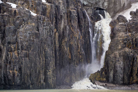 Meltwater waterfall cascading from steep cliffs into icy waters at Alkefjellet, Svalbard