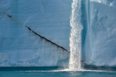 Golden midnight sun lighting a meltwater waterfall arcing over blue ice at Brasvellbreen glacier, Svalbard