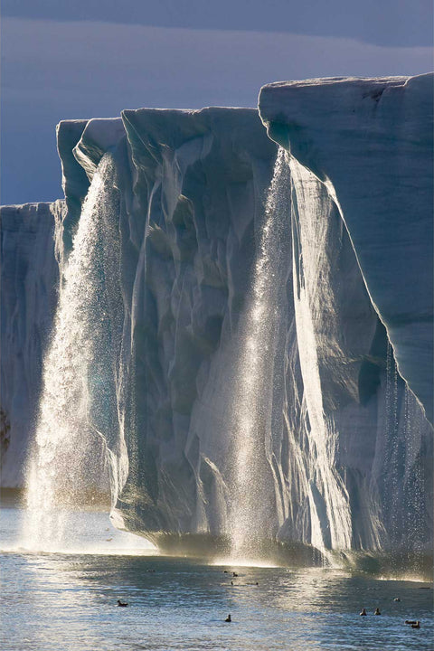Multiple meltwater waterfalls cascading over icy cliffs under midnight sun at Brasvellbreen, Svalbard
