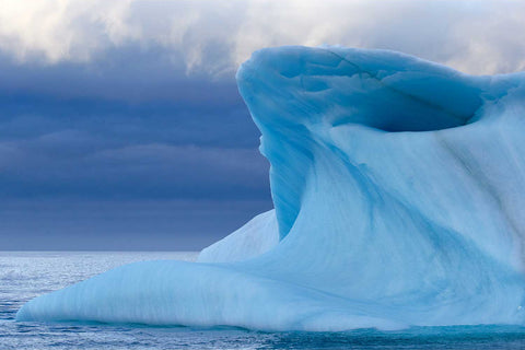 Sculpted blue iceberg rising from Arctic waters under moody skies, Svalbard — fine art landscape photograph by Peter Cox