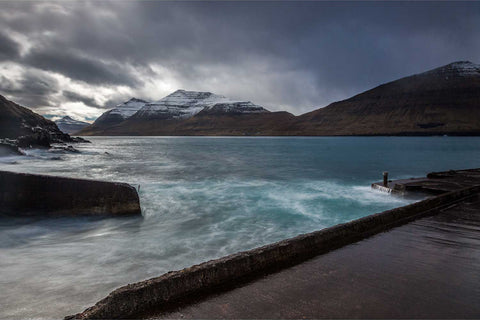 Snow-covered mountains and churning fjord waters with a pier in the foreground, Kunoy, Faroe Islands