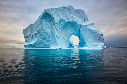 Majestic arched iceberg rising from calm fjord waters in Scoresby Sound, Greenland — fine art landscape photograph by Peter Cox