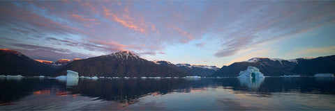 Icebergs drifting in calm waters under a vivid red and pink sunset sky in Scoresby Sound, Greenland with snow-capped mountains