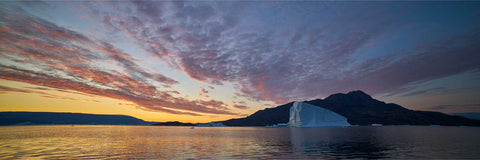 Red and purple twilight sky over Scoresby Sound in Greenland with an iceberg and mountains reflected in calm Arctic waters