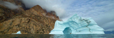 Vivid blue arched iceberg floating beside towering rust-coloured cliffs of Ofjord, Greenland