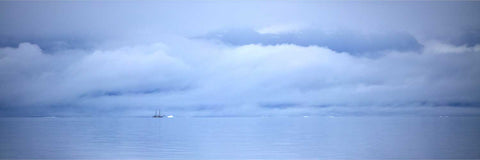 A lone schooner drifting through icy fog across calm blue-grey waters in Greenland