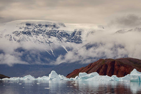 Vibrant red rock of Rodeoe island contrasting with blue icebergs and glaciers in Greenland's Arctic waters