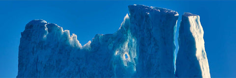 Towering translucent iceberg formations glowing blue-white against a deep blue sky off Greenland