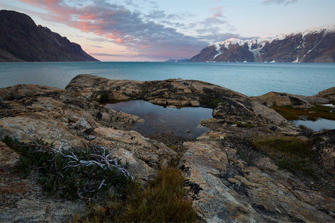 Pink and orange sunrise reflected in a still rock pool at Scoresby Sound, Greenland with dramatic cliffs in the background