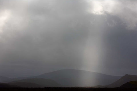 Single beam of sunlight illuminating a hillside through dark storm clouds in Fjallabak Nature Reserve, Iceland