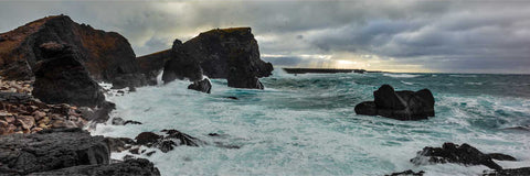 Storm waves crashing against dark basalt sea stacks at Reykjanesta, Iceland with turquoise water and dramatic sky overhead