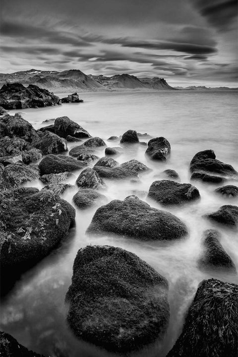 Black and white long exposure of coastal boulders in soft water at Budir, Iceland, fine art landscape photograph by Peter Cox