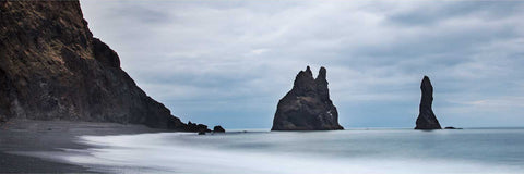 Long exposure of the Reynisdrangar sea stacks rising from black sand beach at Reynisfjara, Iceland with softened waves under overcast sky