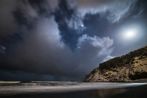 Reynisfjara sea stacks under moonlight and a starry winter sky on Iceland's black sand beach