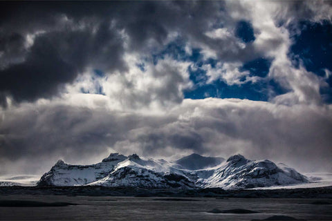 Snow-blanketed mountains under moonlight with stars at Jokulsarlon Glacier Lagoon, Iceland