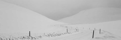 Black and white panoramic of a snowy road stretching to the horizon between snow-covered hills, Iceland