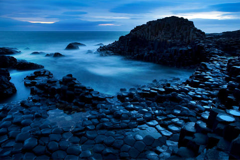 The Giant's Causeway at twilight with wet hexagonal basalt columns stretching to the sea and long exposure blurred waves
