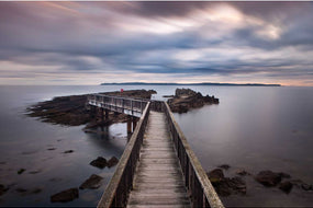 Long exposure of Pan's Rock with its footbridge at dawn on the Antrim Causeway Coast, silky water and blurred clouds, Rathlin Island on the horizon