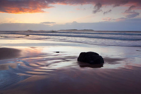 Sunset over the Skerries coast in County Antrim with warm light reflecting on wet sand and rock formations