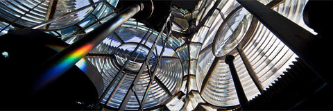 Inside the rotating lantern of the Fastnet Lighthouse with Fresnel lenses, ladder, and a rainbow projected on a pole