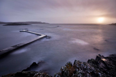 Long exposure of a small pier extending into a bay at sunset under heavy cloud, Lehanbeg, Cork
