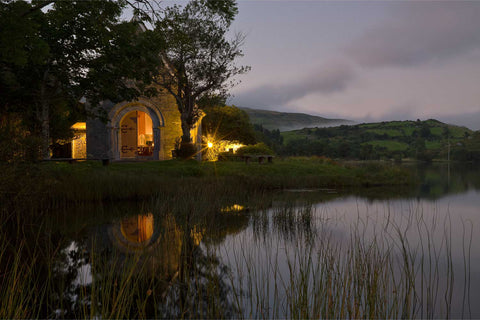 St. Finbar's Oratory glowing warmly on its island in Gougane Barra lake at twilight with calm reflections in the water