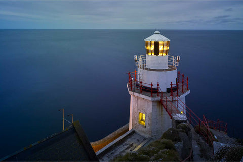 Bull Rock Lighthouse illuminated at night against the Atlantic with long exposure smoothing waves and clouds into soft textures